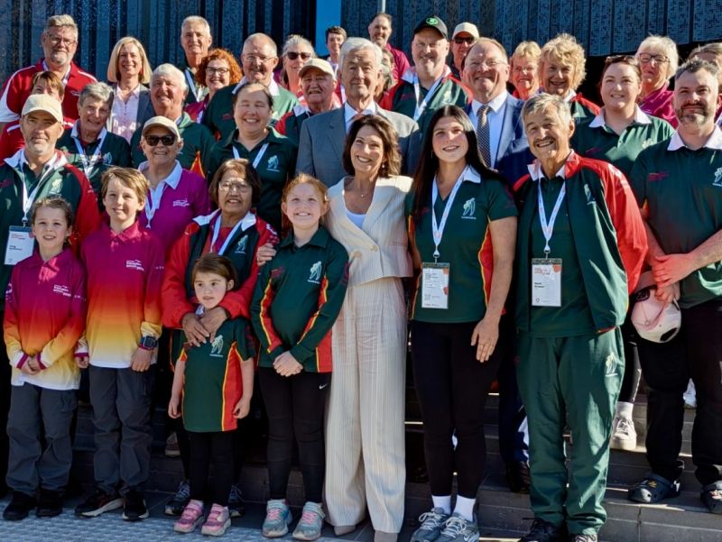 The Governor and Dr Walters stand outdoors with a large group of people in green and red uniforms
