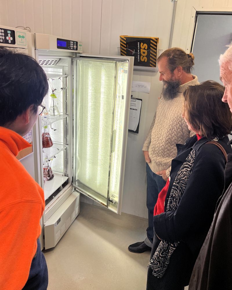 The Governor and Dr Walters stand with two men indoors looking at a fridge containing seaweed samples