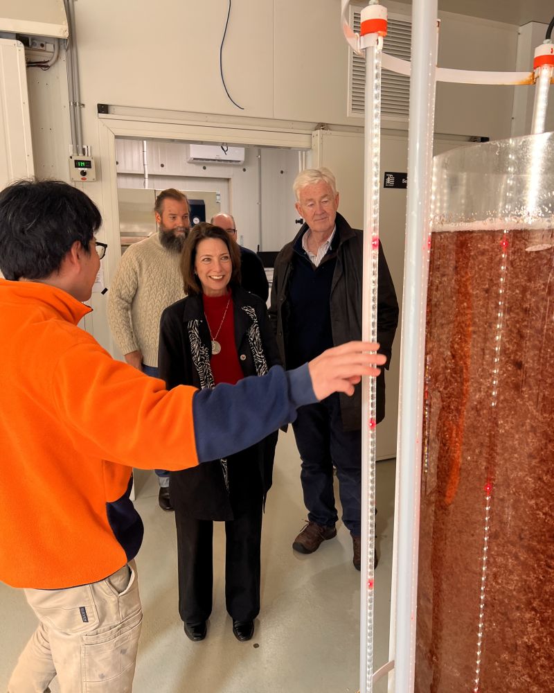 The Governor and Dr Walters stand indoors in an industrial facility looking at a tank of seaweed