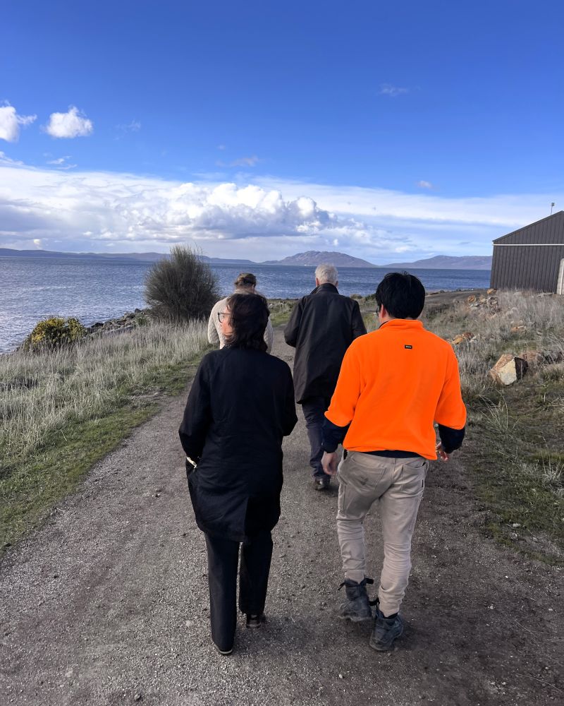 The Governor and Dr Walters walk outdoors with two men on a pathway next to a coastline
