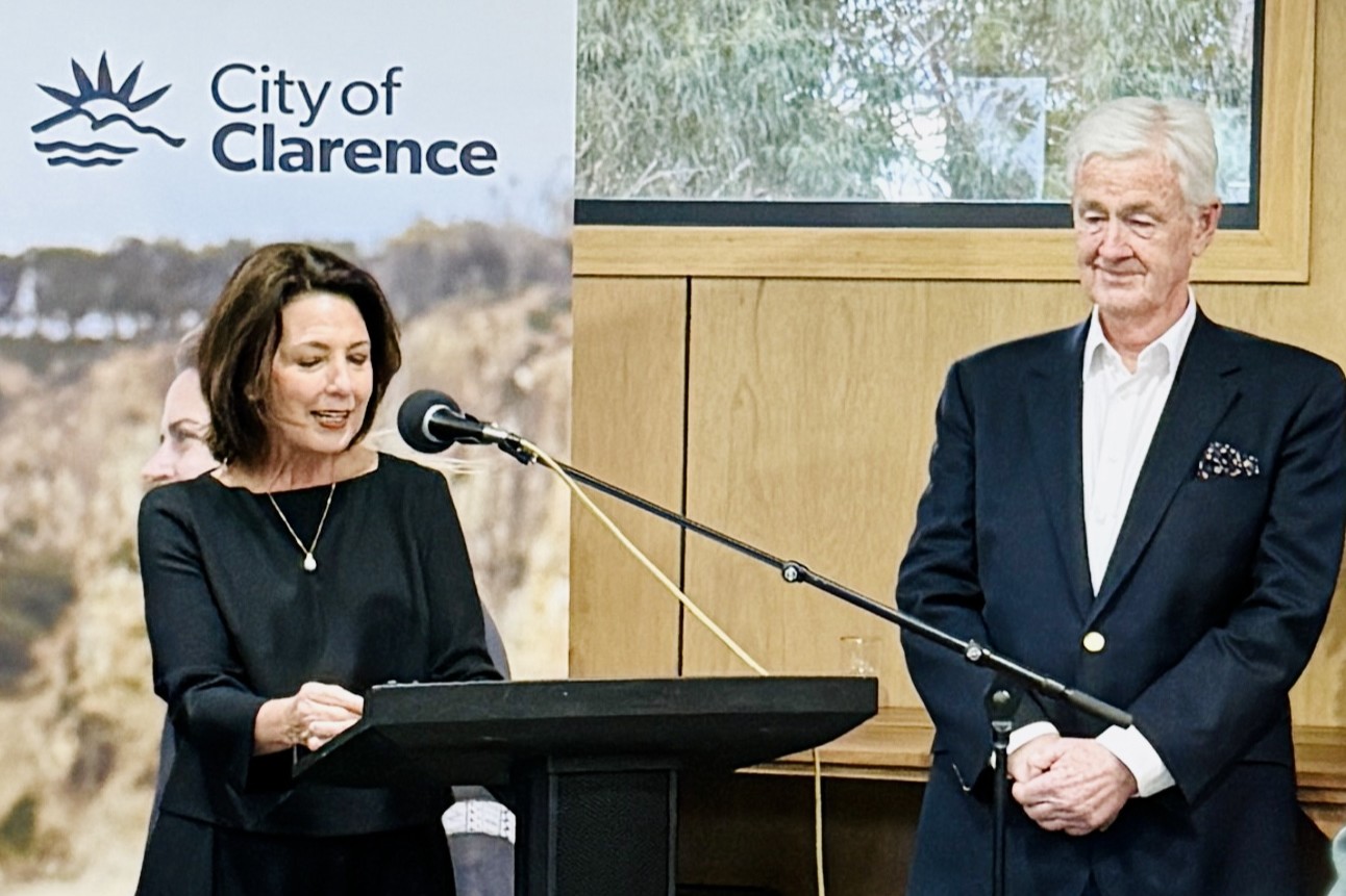 The Governor stands indoors at a lectern, in front of a banner reading 'City of Clarence'. Dr Walters stands next to her.