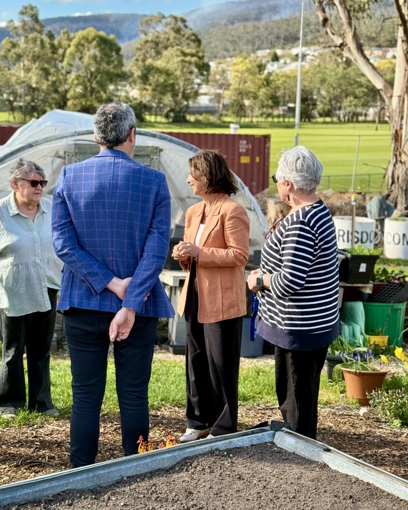 The Governor stands outdoors with a group of people in a community garden