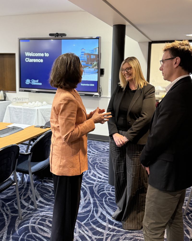The Governor stands in a conference room speaking to two people