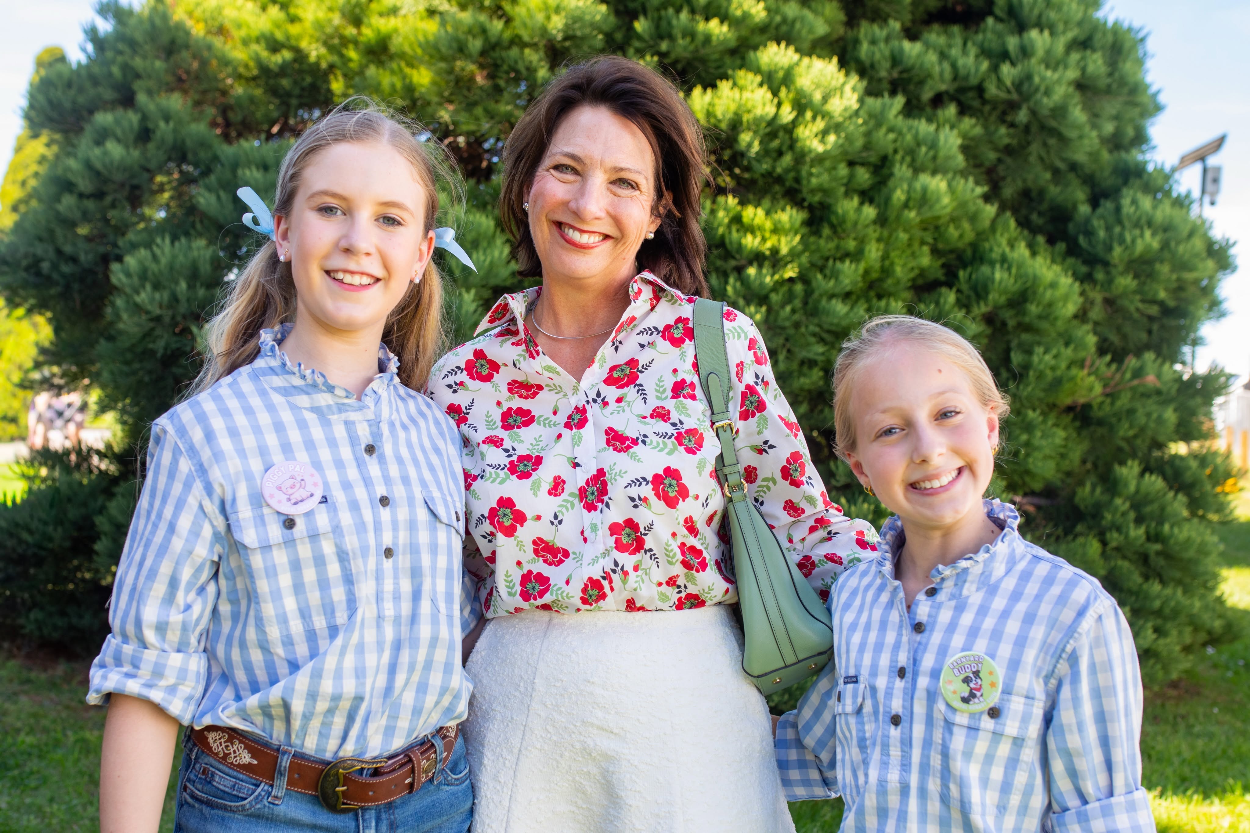 The Governor stands with two young girls who are wearing blue checked shirts. Everyone is looking at the camera and smiling,