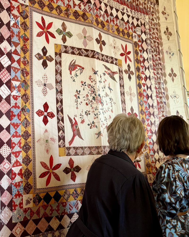 Two people with their backs to camera look at a large colourful quilt on display