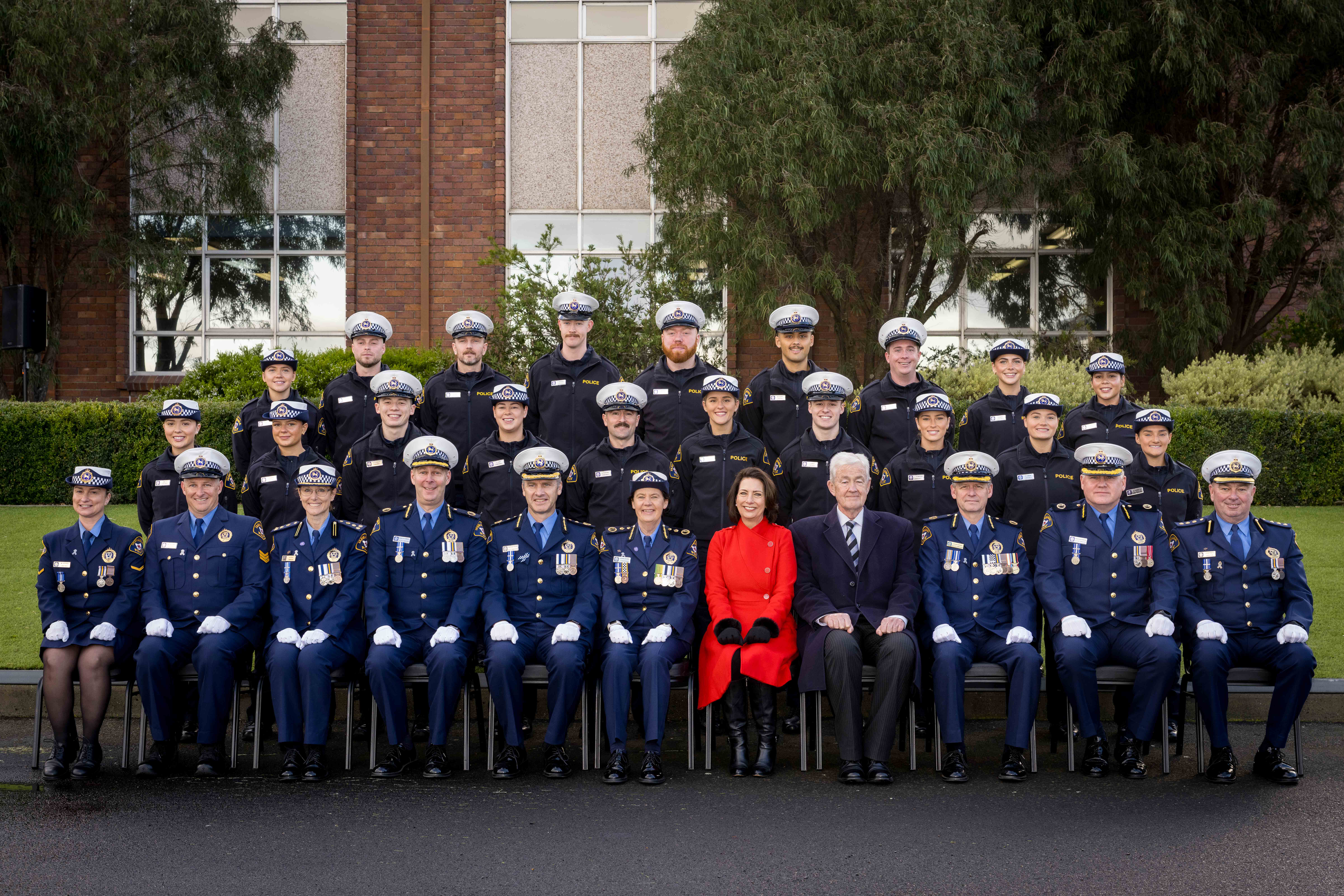 The Governor and Dr Walters sit with a group of 28 Tasmania Police officers outdoors. Everyone is looking at the camera and smiling.