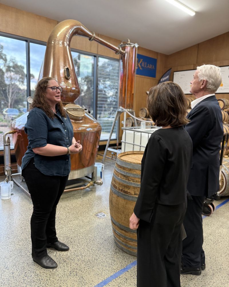 The Governor and Dr Walters stand next to a whisky still talking to a woman