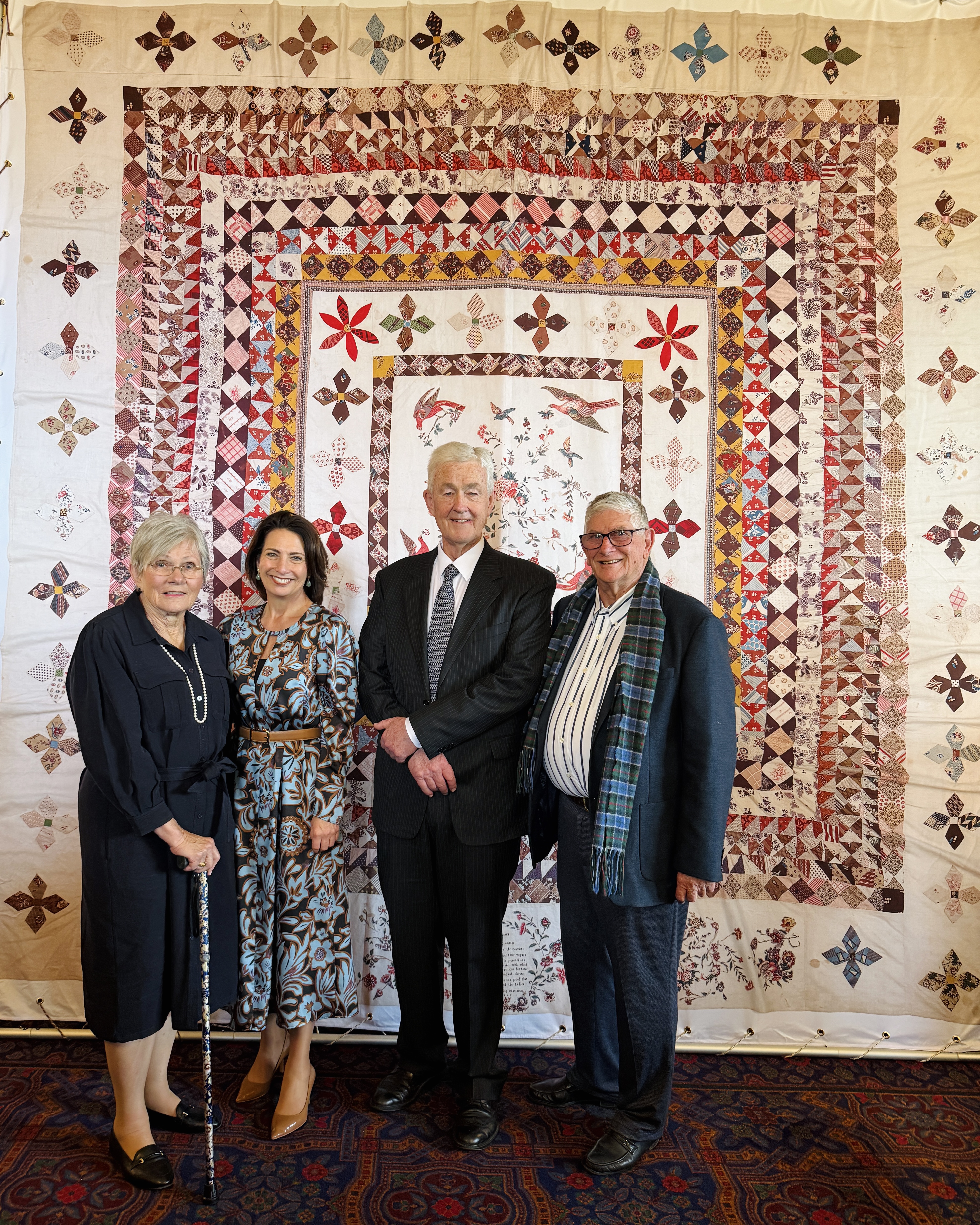 The Governor and Dr Walters stand with a man and a woman in front of a large colourful quilt. Everyone is looking at the camera and smiling.