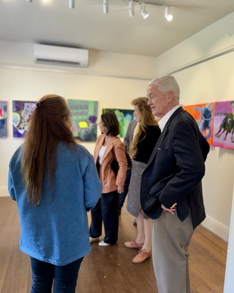 Dr Walters speaks to a woman inside an art gallery, while in the background the Governor speaks with a group of people