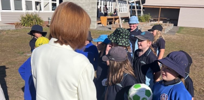 Her Excellency with a group of school children standing in front of a school building