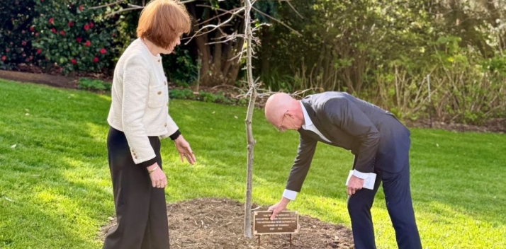 Peter Gutwein placing a plaque next to an oak tree while Her Excellency watches on